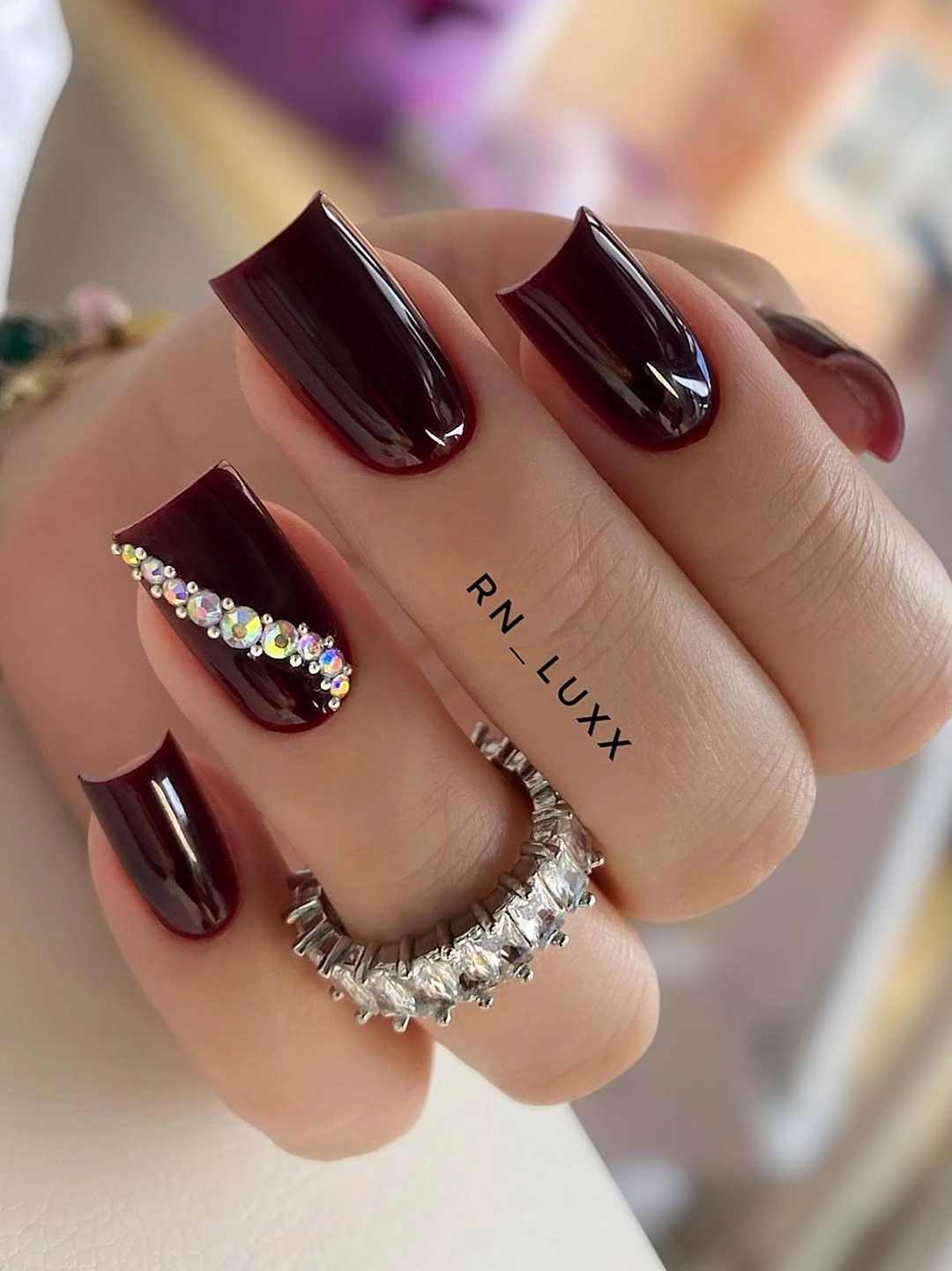 Glossy burgundy square nails with a narrow rhinestone accent line