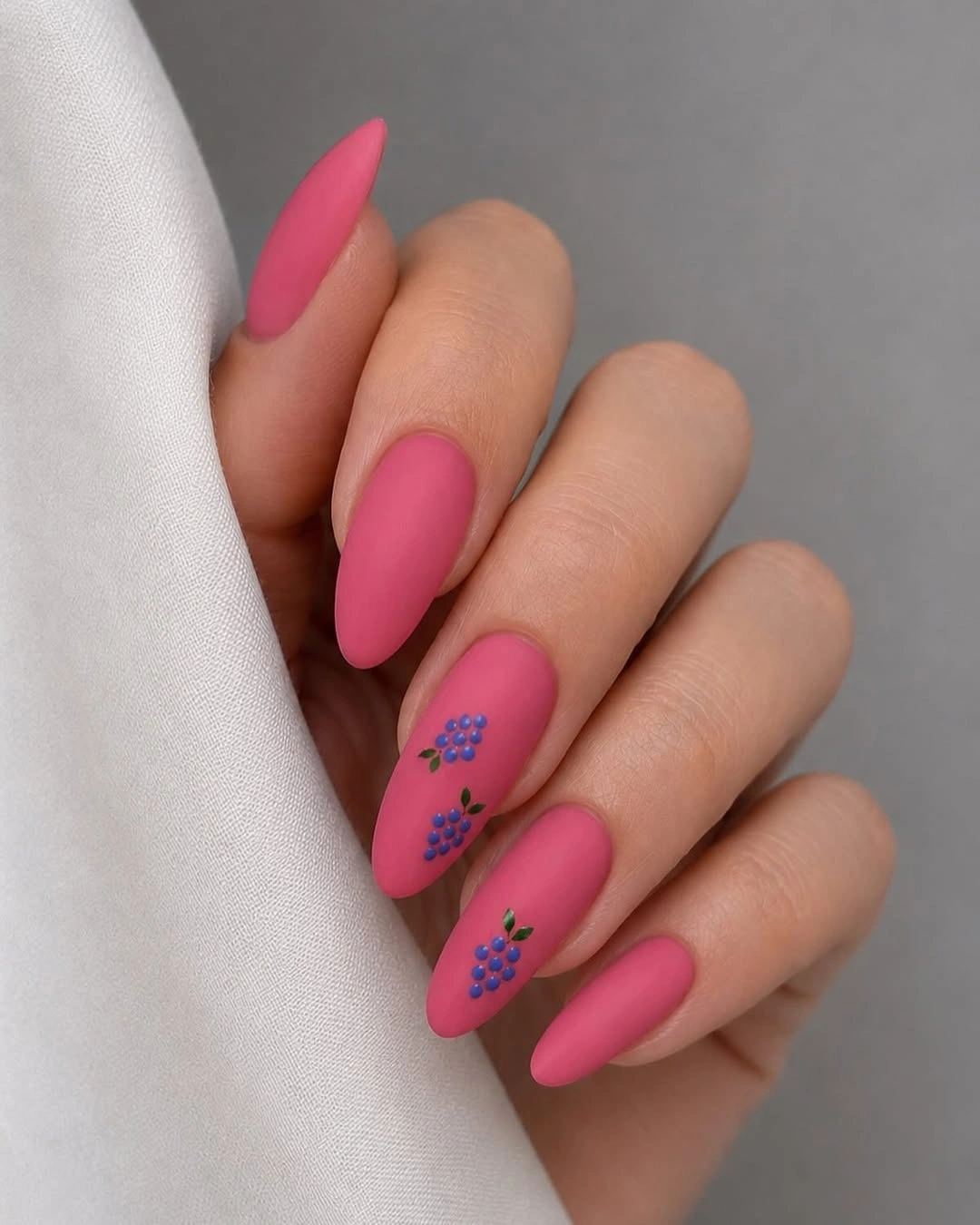 Matte hot pink almond nails with tiny blue floral accents