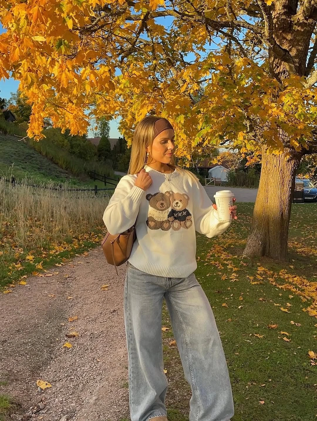 White teddy motif sweater with faded wide-leg jeans brown headband and bag