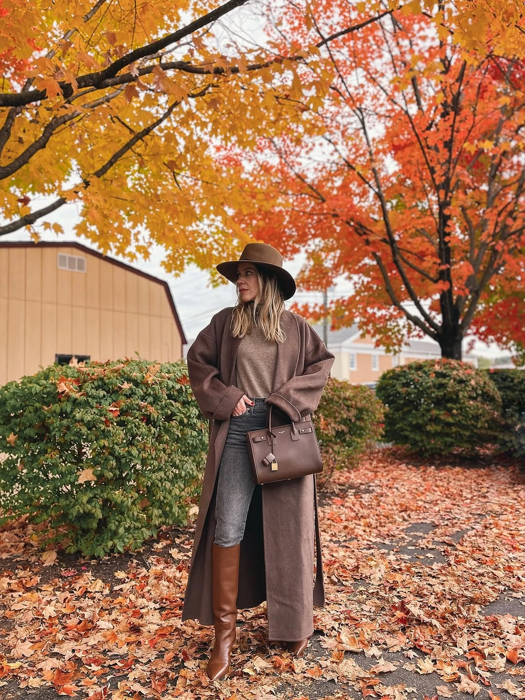 Long brown coat with gray jeans tall boots and wide-brim hat