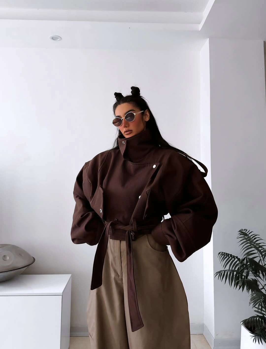 Chocolate belted high-collar jacket with wide taupe trousers and round sunglasses