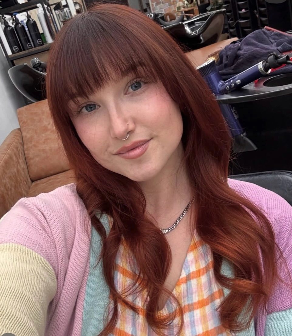Deep copper-brown hair with full blunt fringe and softly curled lengths
