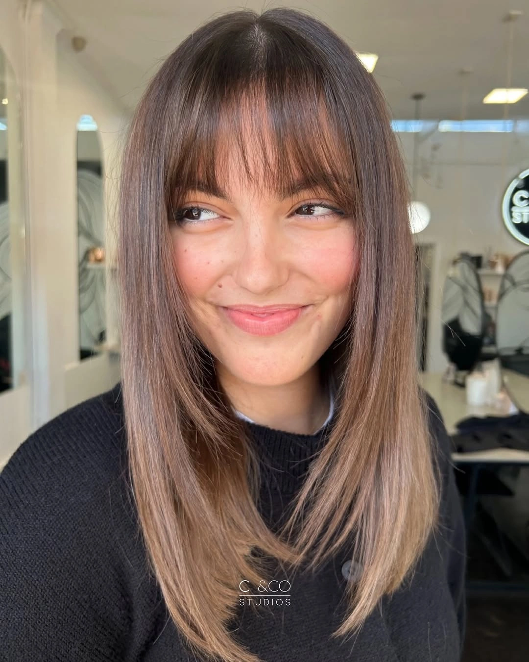 Long muted brown hair with wispy full fringe and softly curled ends
