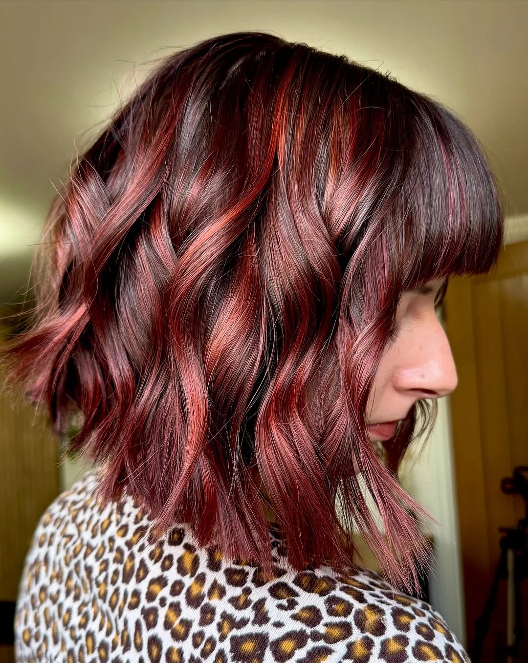 Short deep burgundy bob with blunt fringe, tousled waves, and uneven ends