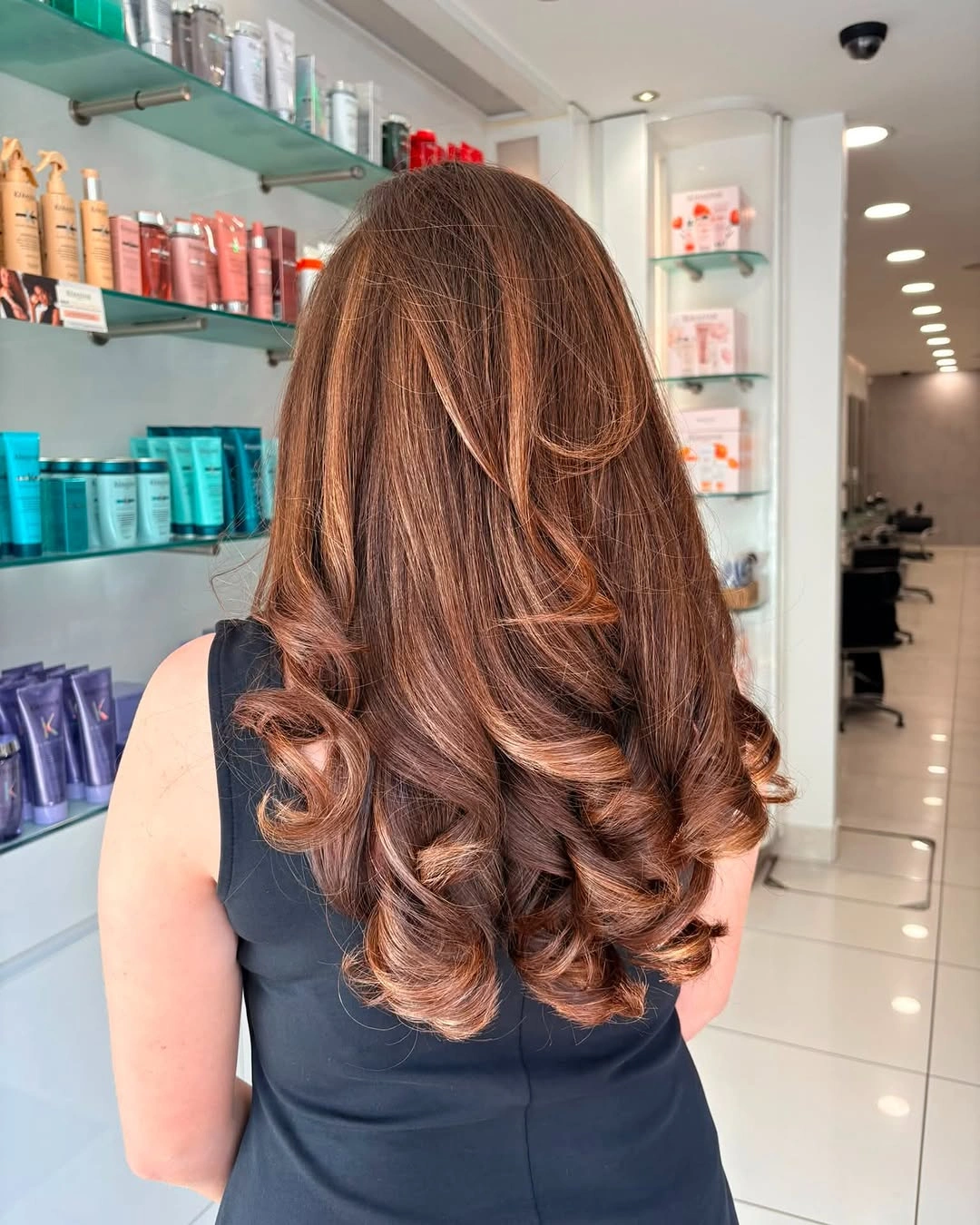 Long chestnut-brown hair with polished lower curls and subtle layers