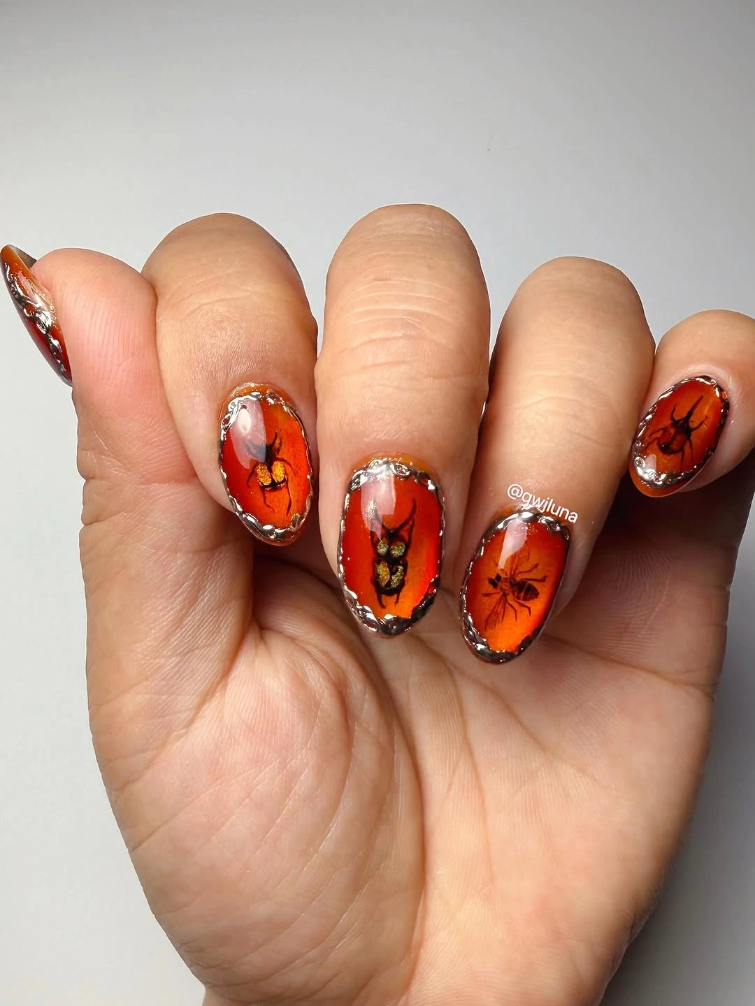 Bright orange oval nails with black botanical lines and silver edge