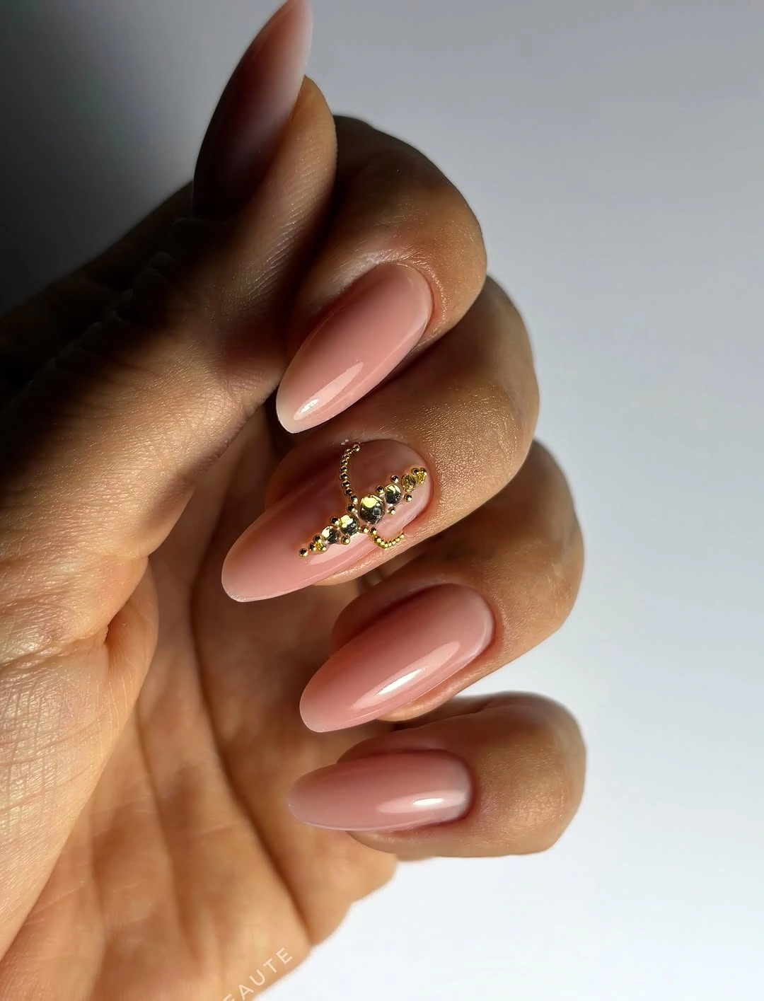 Soft nude almond nails with one small gold seasonal accent
