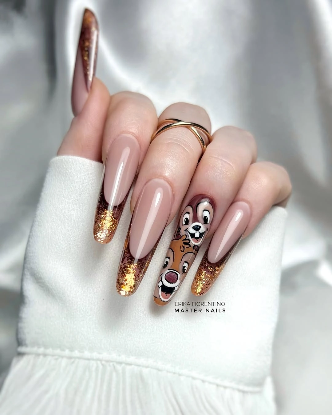 Pale nude almond nails with gold glitter tips and dog accent
