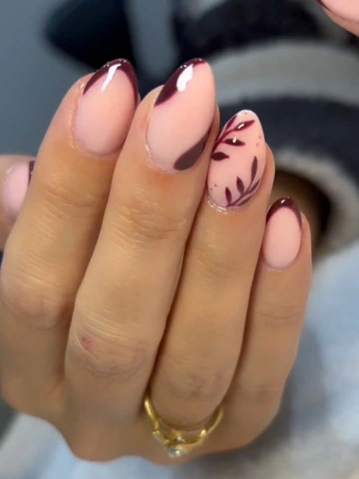 Milky pink almond nails with burgundy French tips and leaf art