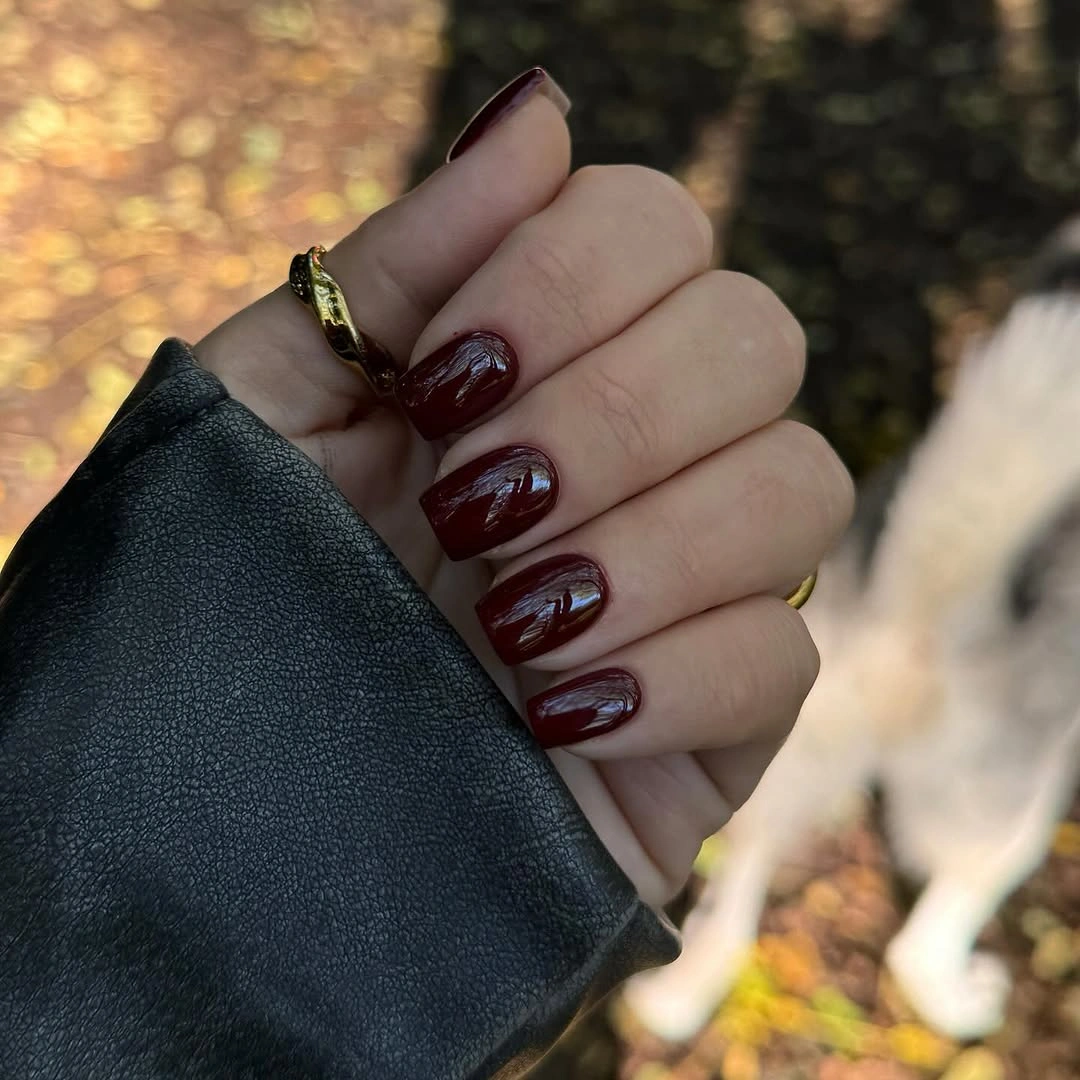 Short glossy wine red almond nails with a minimal light accent
