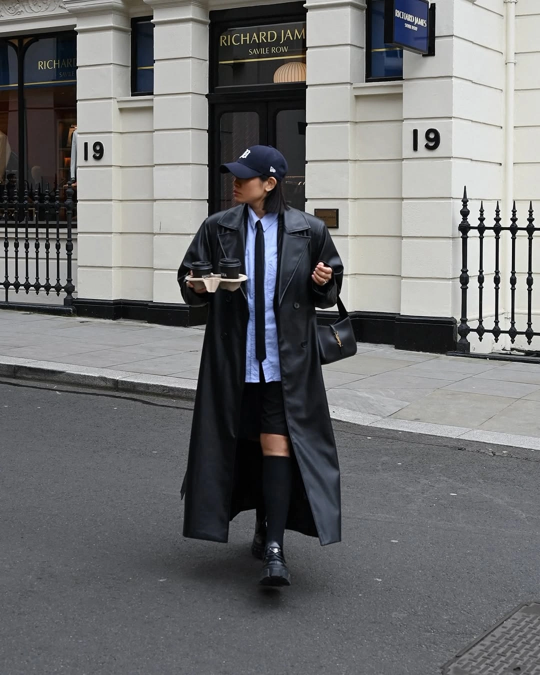 Long black coat with cap knee socks loafers and shoulder bag