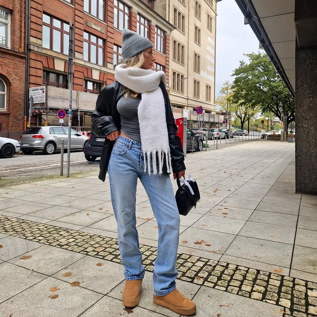 Black leather look jacket with white scarf blue jeans and tan boots