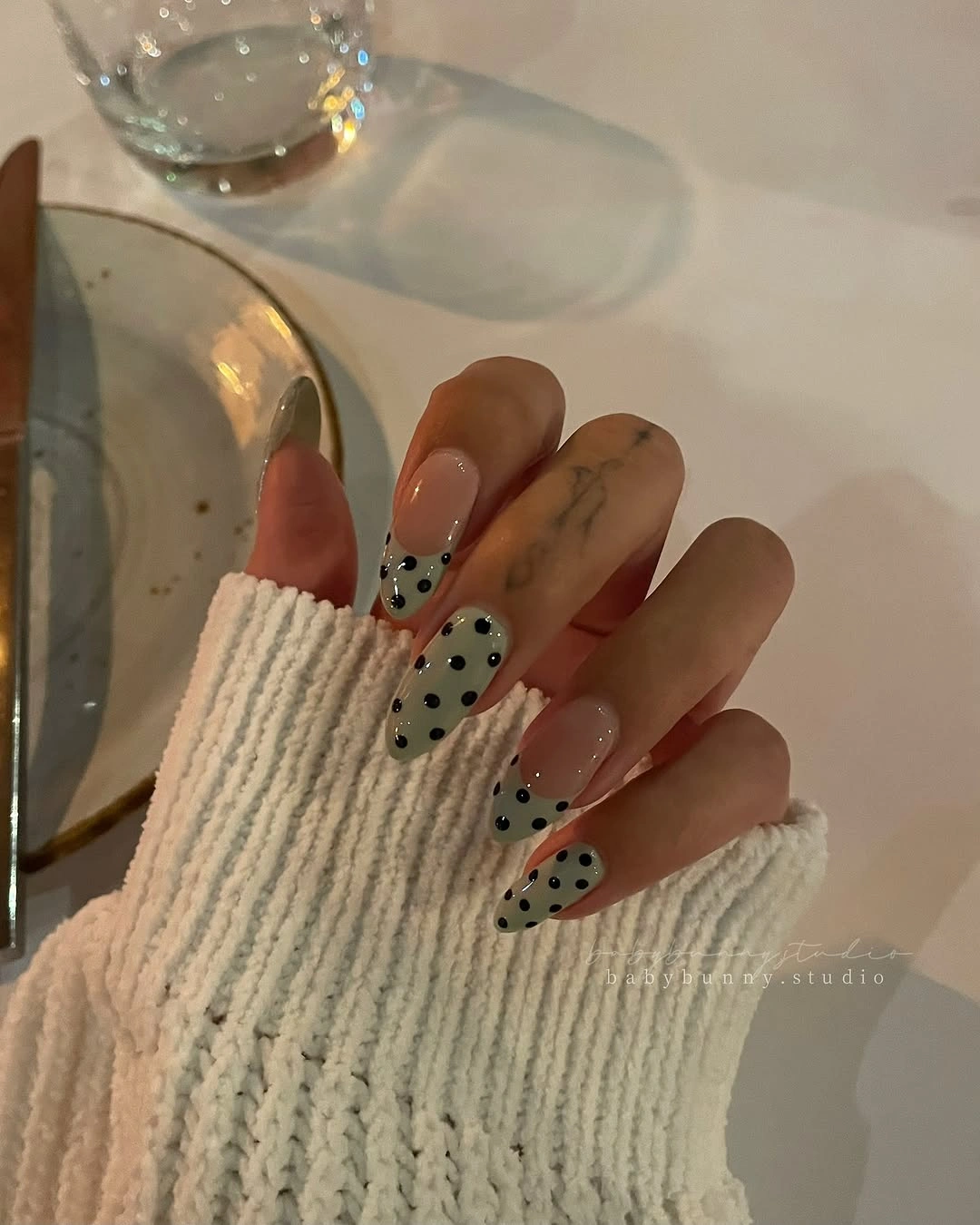 Sheer nude almond nails with sage green tips and black dots
