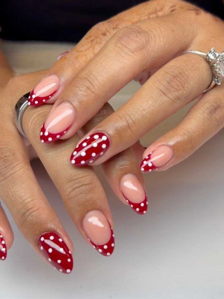 Nude oval nails with red curved tips and white dot clusters