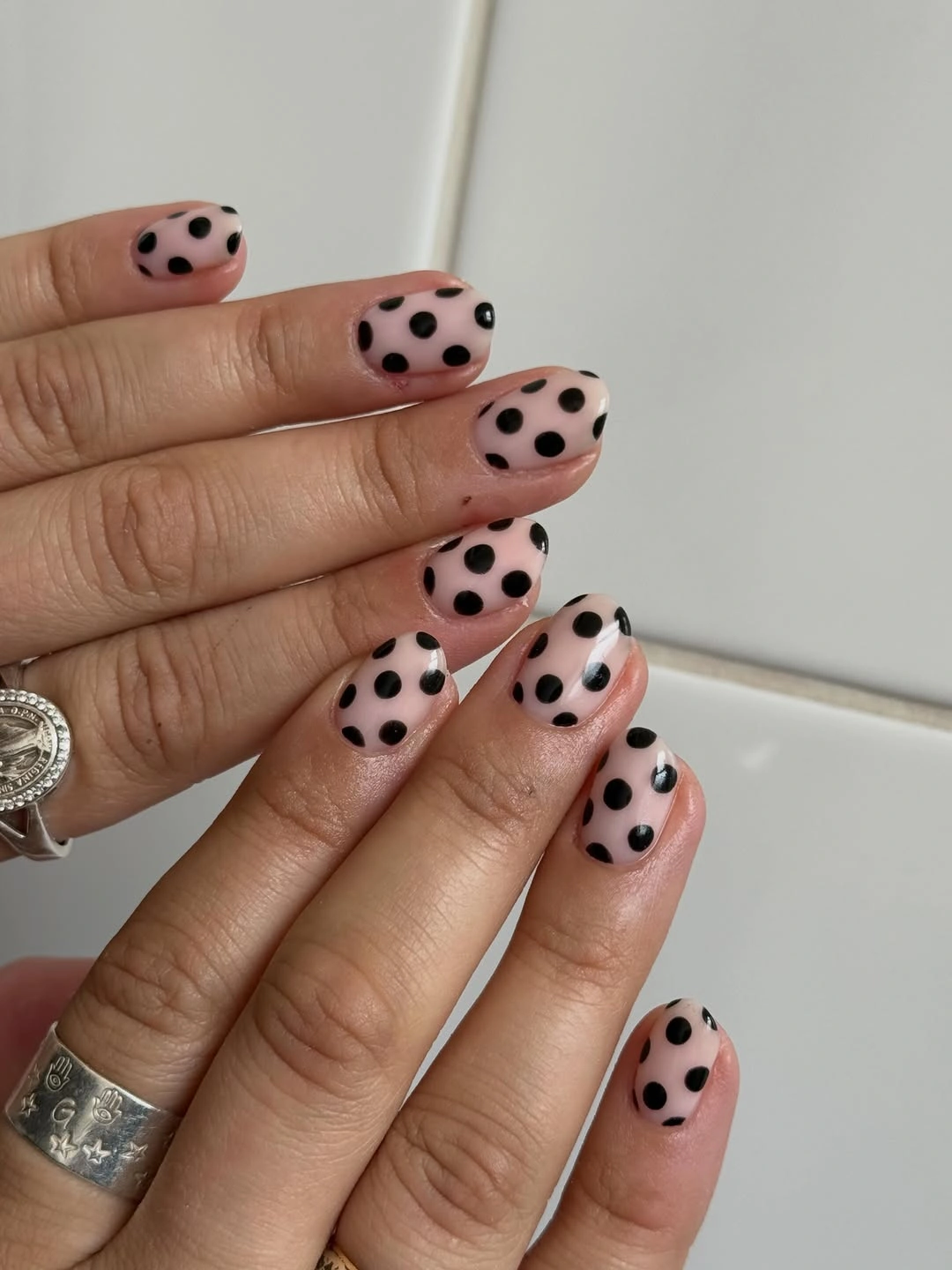 Short pale pink rounded nails with irregular black polka dots