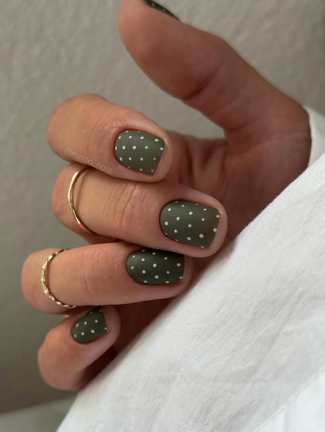 Short muted olive nails with fine white polka dots
