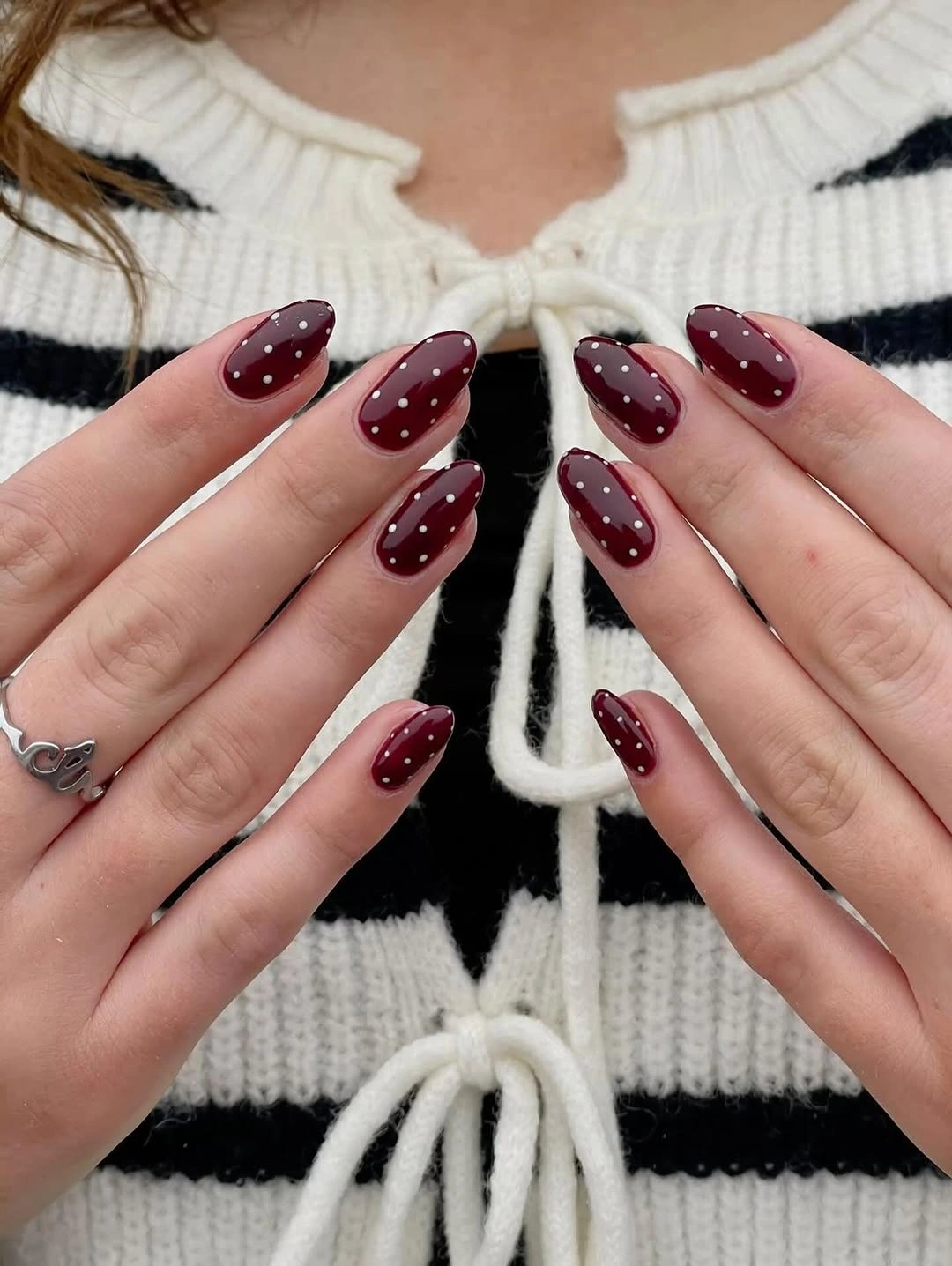 Long burgundy almond nails with small white dots near edges