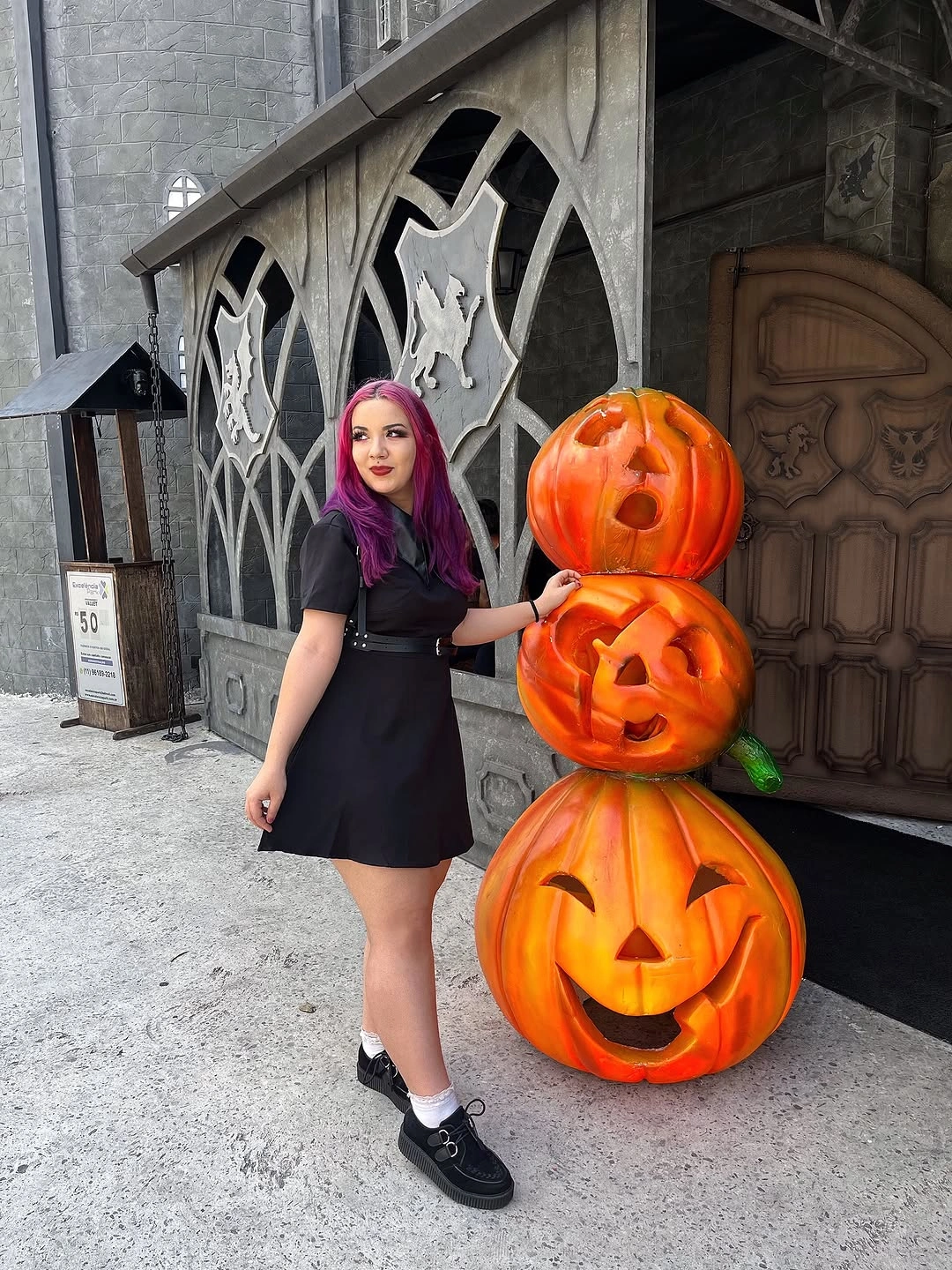 Black mini dress Halloween outfit with pink hair and black loafers beside pumpkins