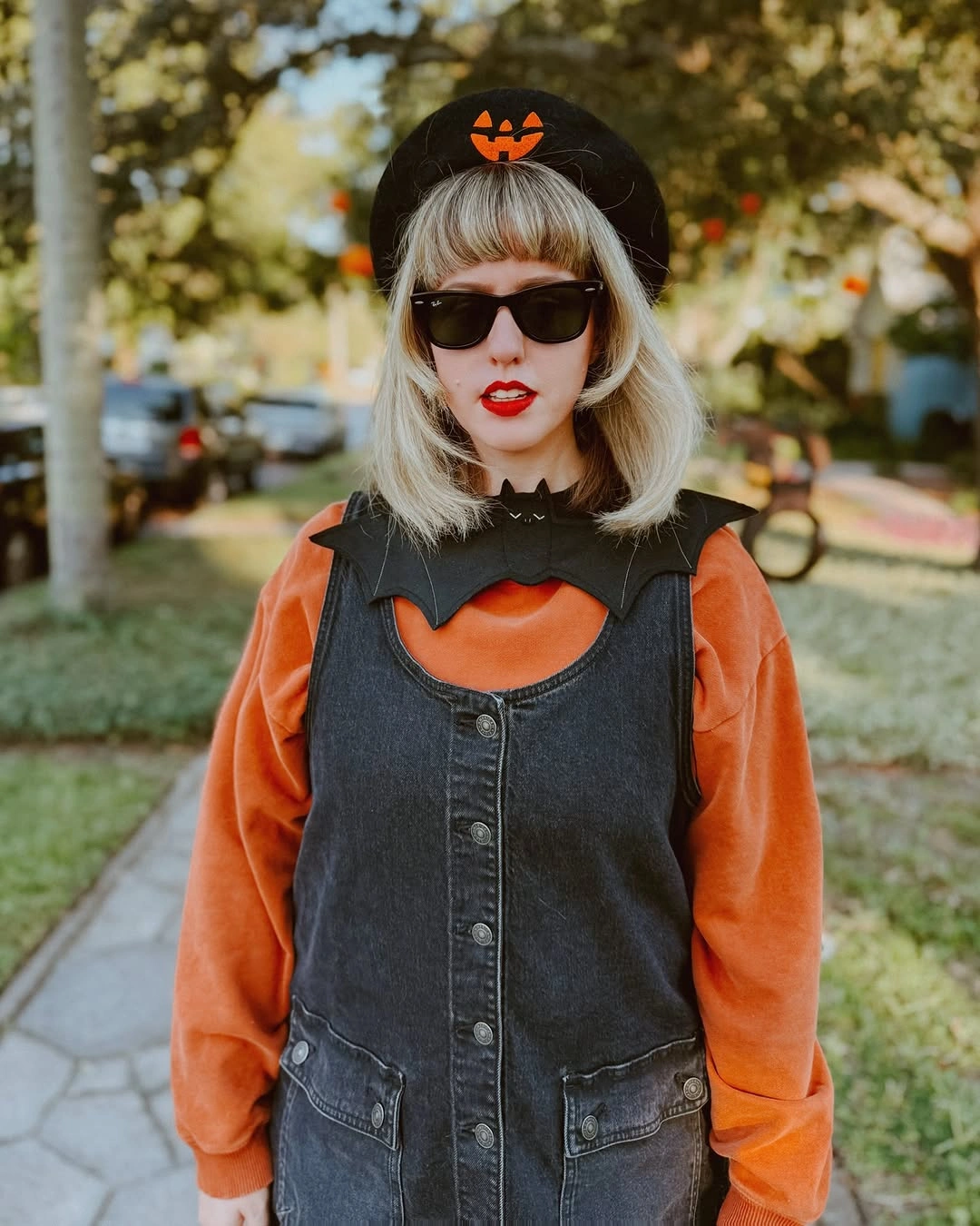 Orange long-sleeve top under black vest with pumpkin hair accessory and sunglasses