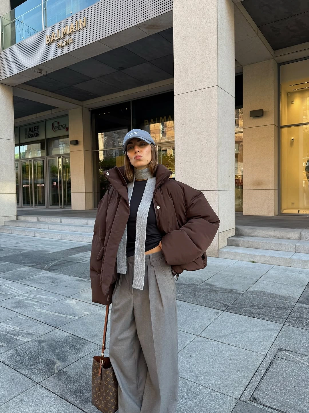 Brown puffer with gray scarf, cream trousers, and cap for work