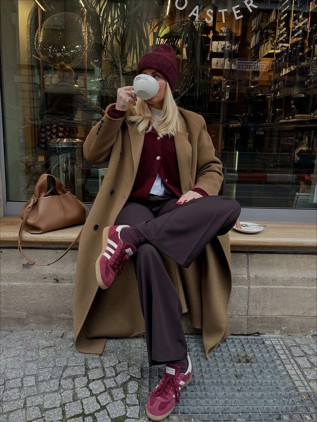 Camel coat with burgundy knit, dark trousers, and burgundy sneakers