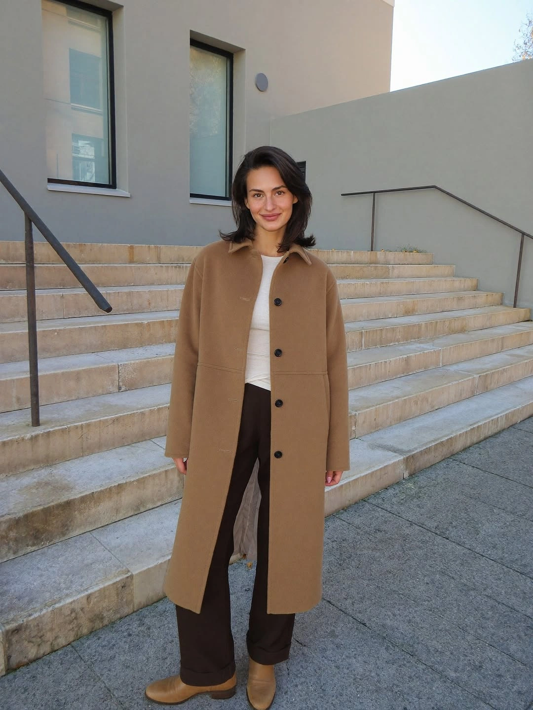 Camel coat with cream cardigan, brown trousers, and tan shoes