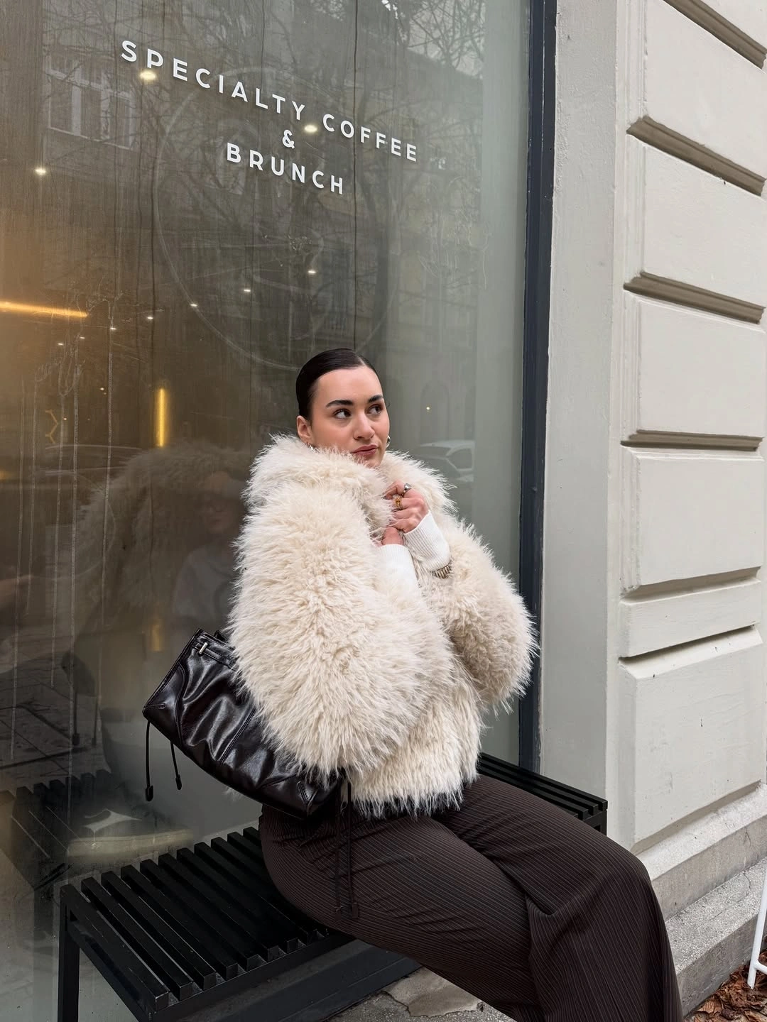 Ivory shaggy coat dark pinstriped trousers and black tote