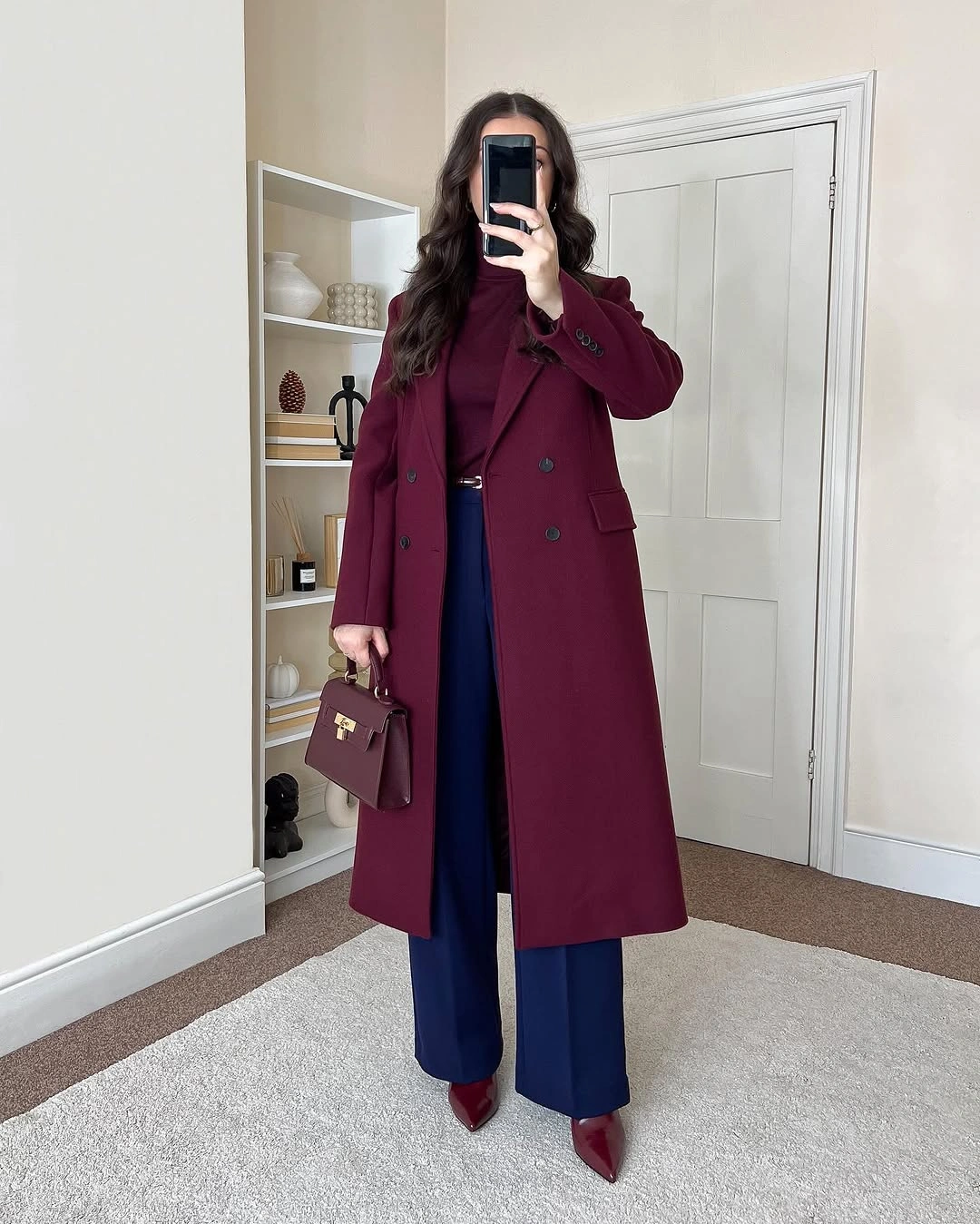 Burgundy coat, dark red top, blue trousers, pointed shoes, handbag