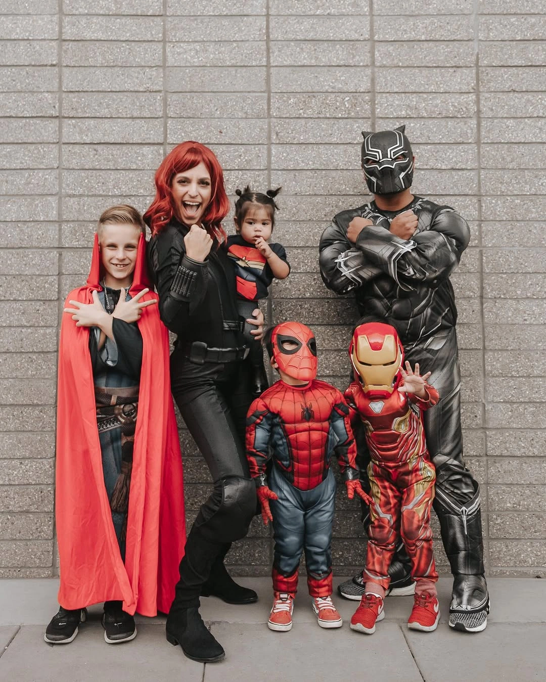 Family in red and black comic hero costumes with baby