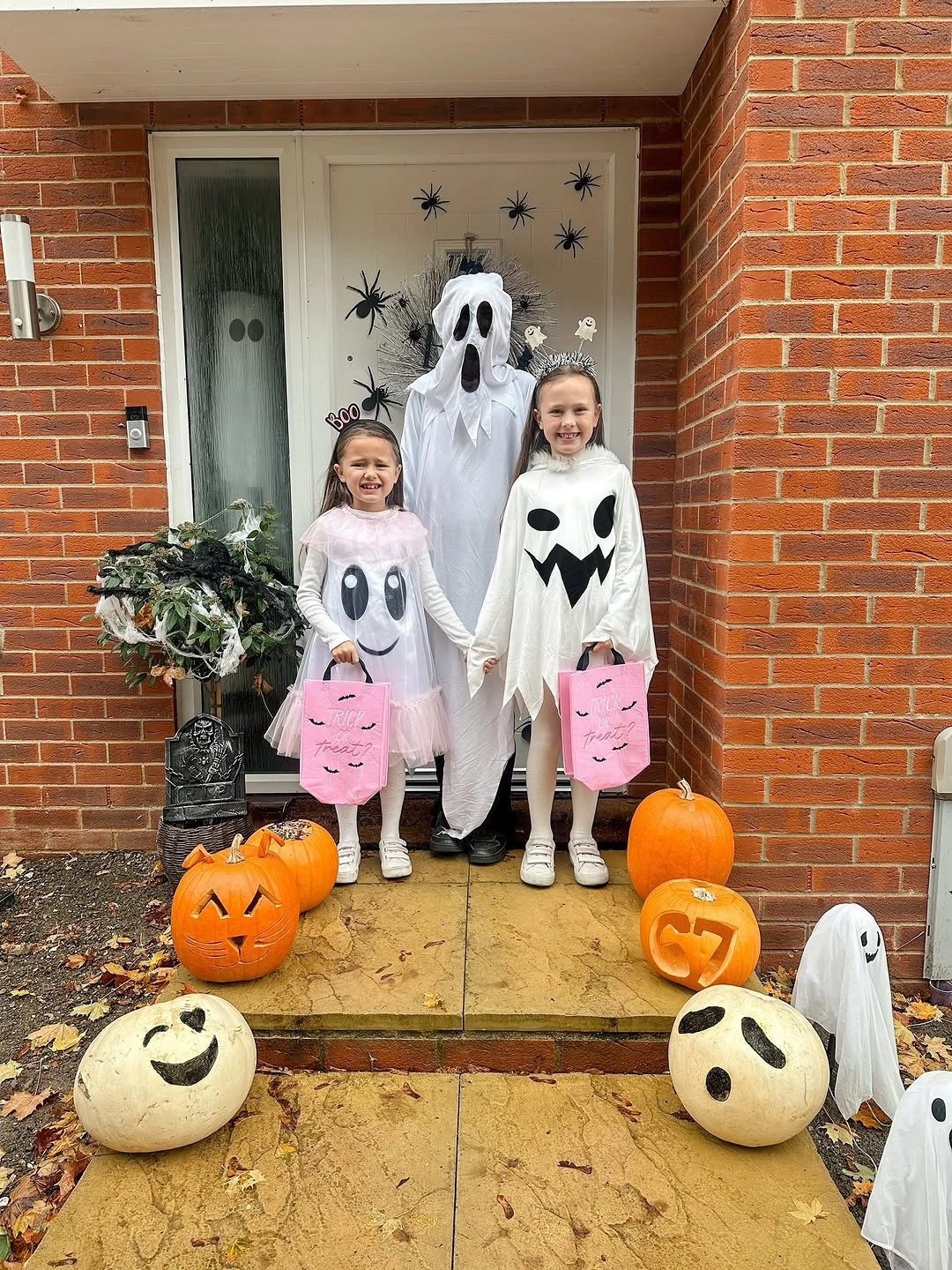 Three children in white ghost costumes at decorated doorway