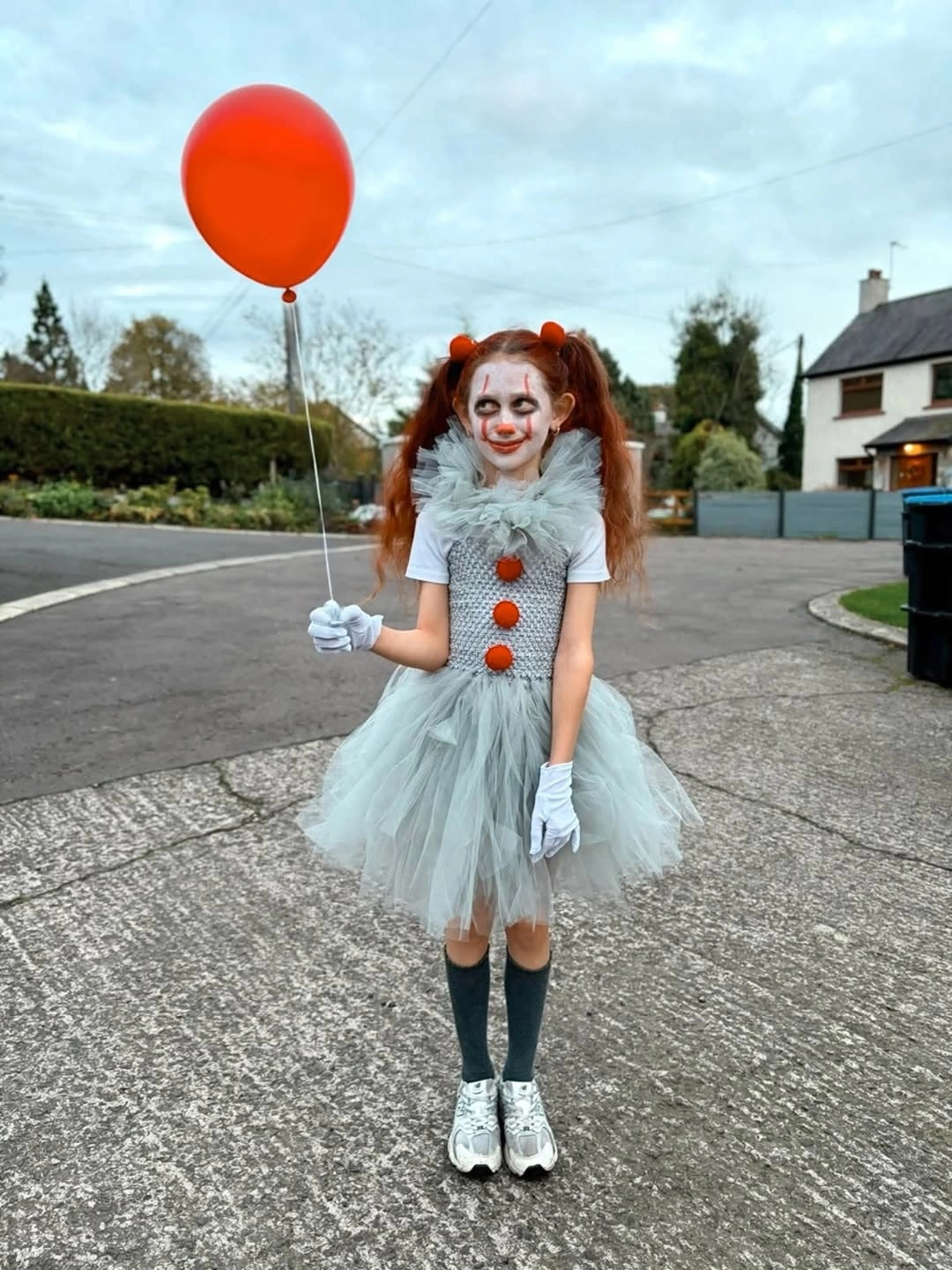 Girl in pale blue clown dress with red pom-poms and balloon