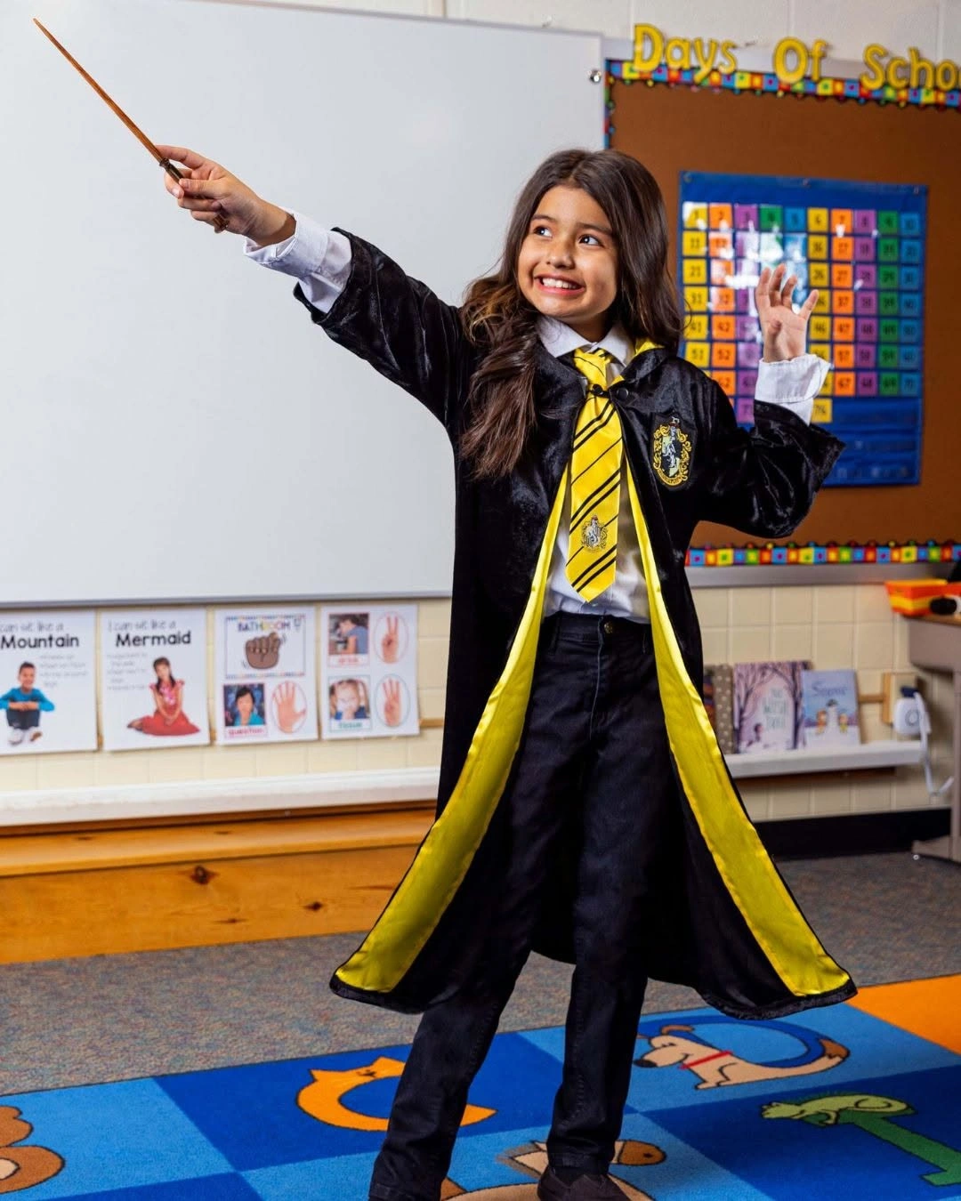 Girl in black school robe with yellow trim and wand