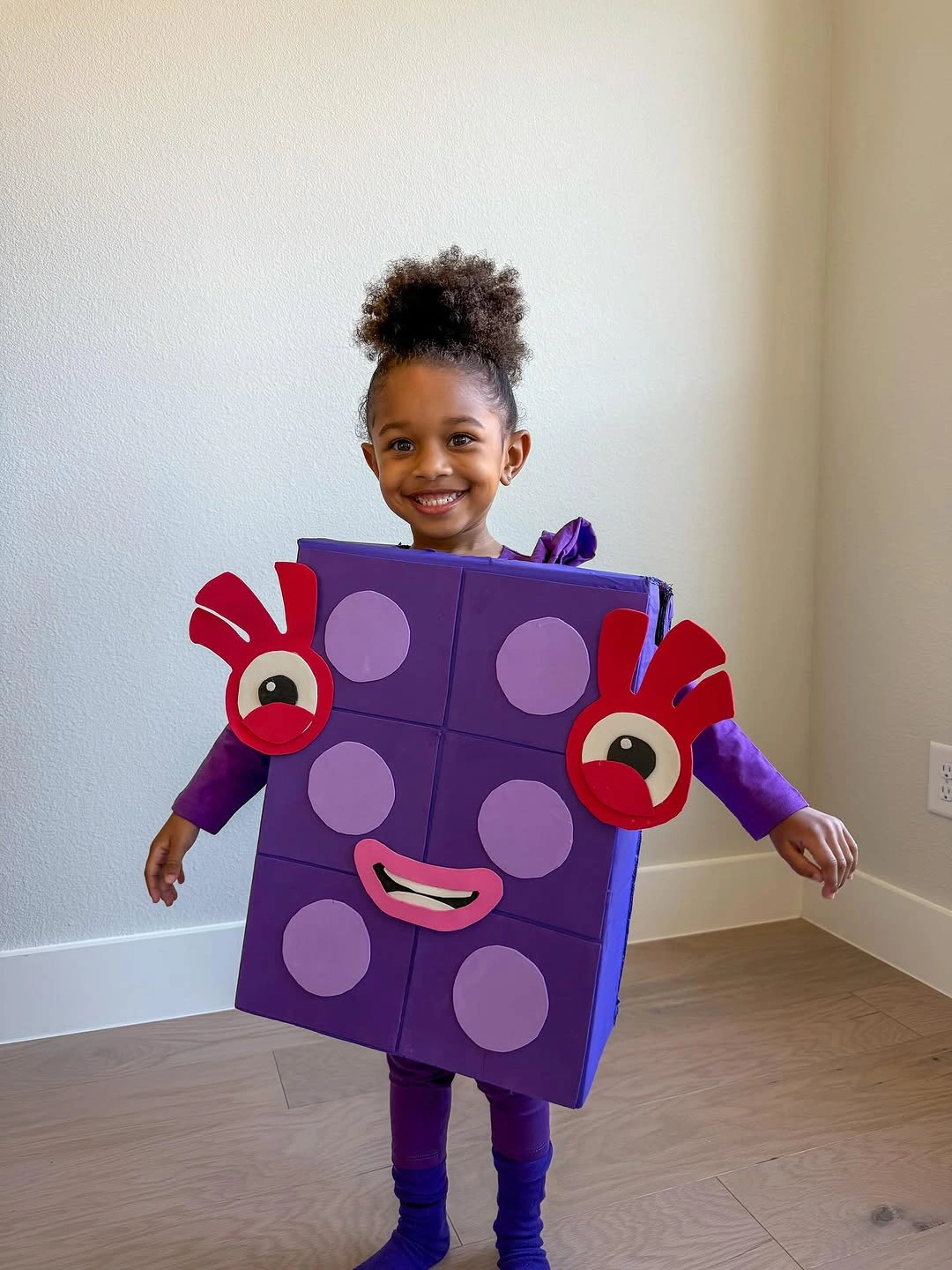 Girl in oversized purple dice box costume with red details