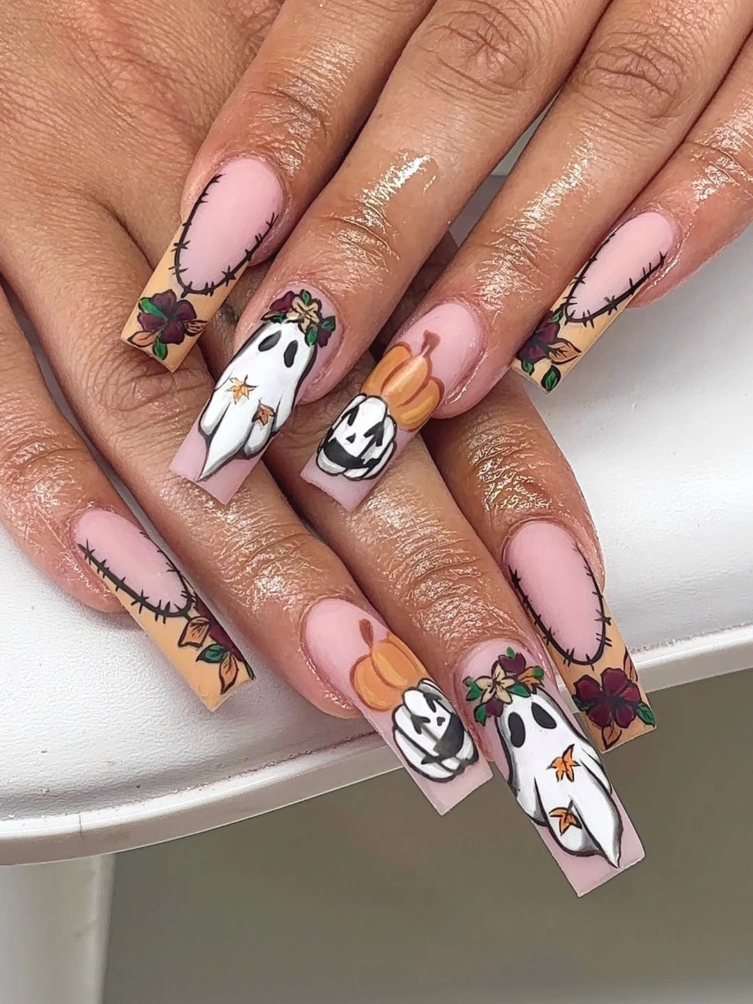 Long pink square nails with ghosts pumpkins flowers and stitch lines