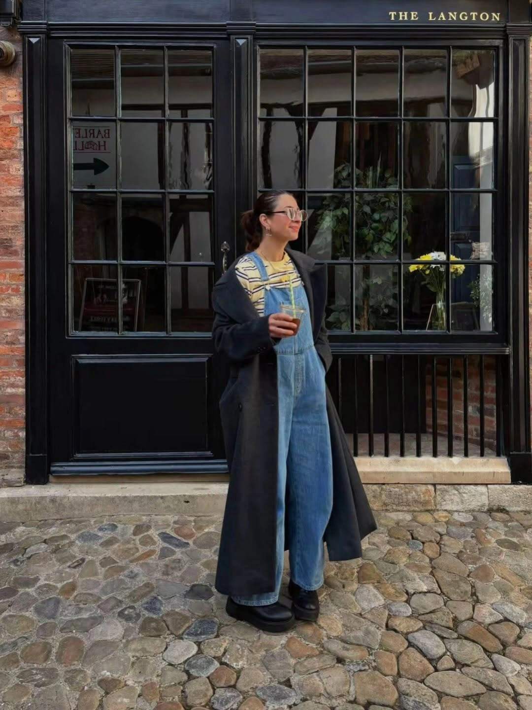 Long dark coat over light denim overalls and striped top