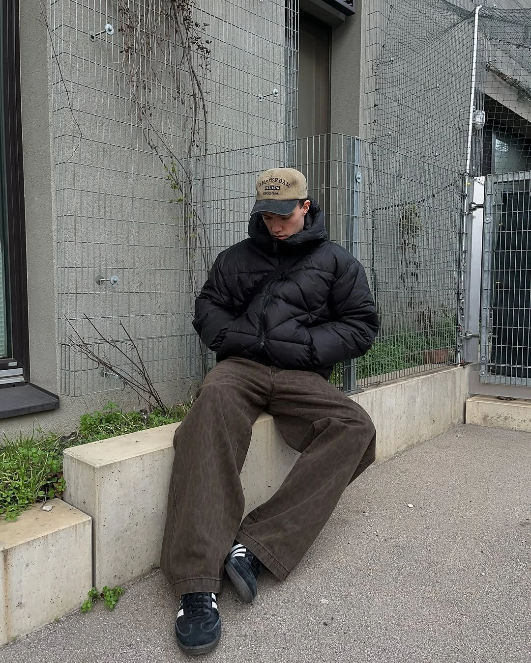 Black puffer jacket with loose brown trousers and dark cap