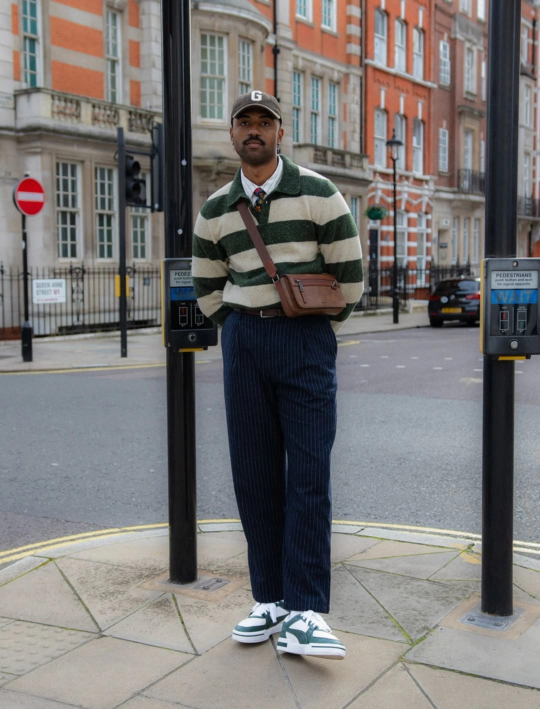 Green striped rugby top with navy pleated trousers and white sneakers