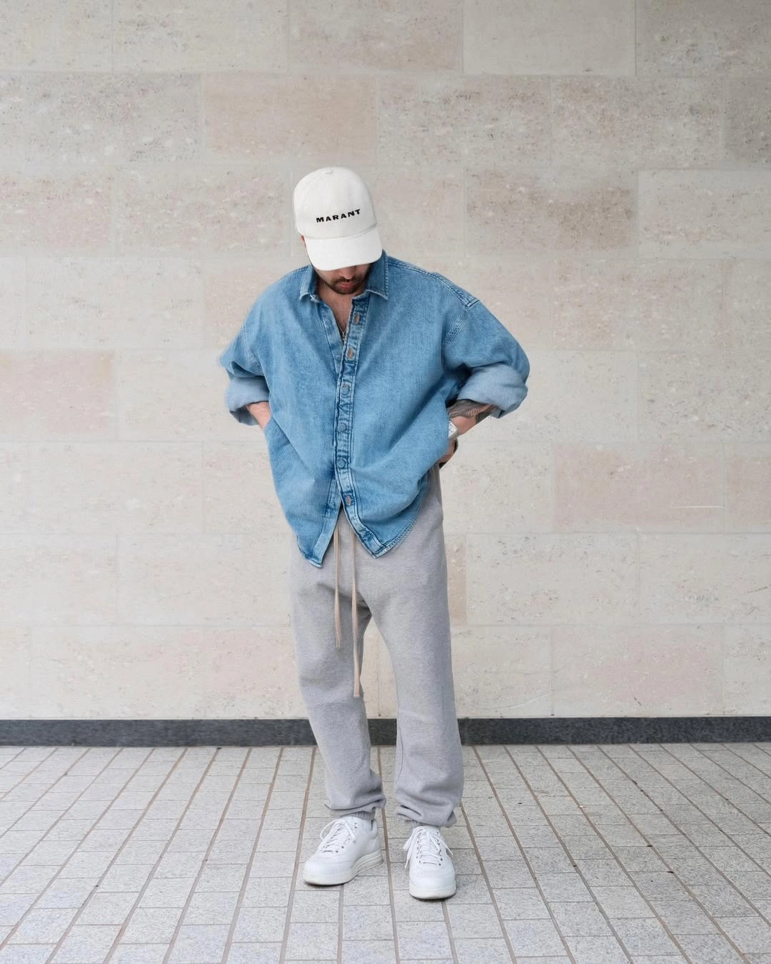 Washed denim shirt with gray relaxed pants, white cap, and sneakers