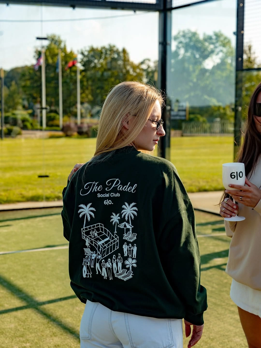 Black graphic sweatshirt with short white skirt at a padel court