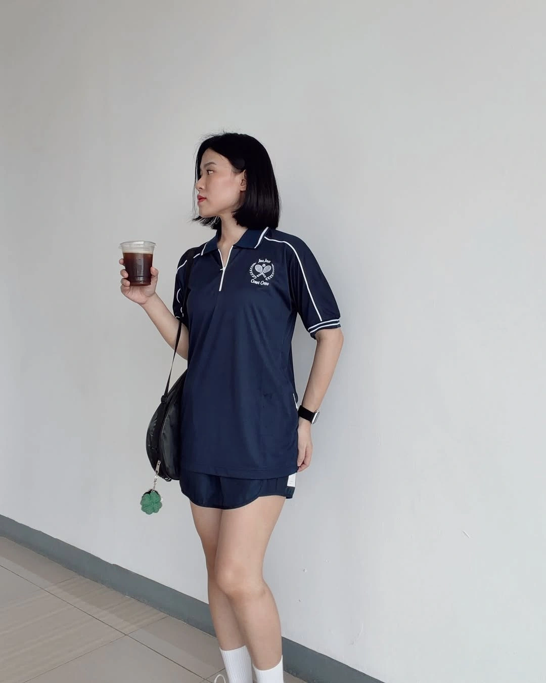 Navy polo dress with white socks and crossbody bag near padel court