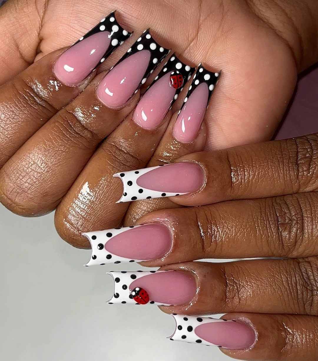 pink almond French nails with white dots and a ladybug accent