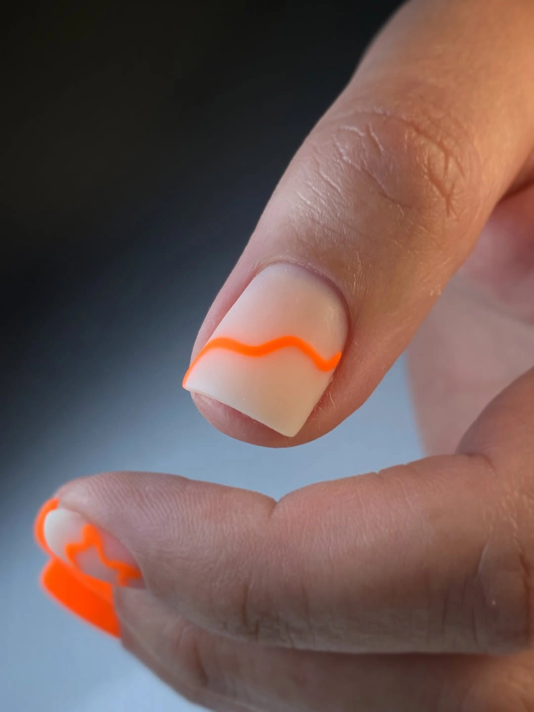 Very short milky nails with neon orange wavy tips