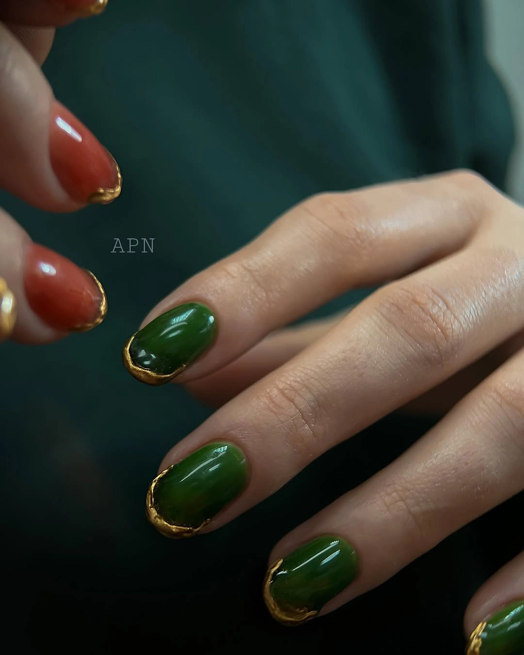 Glossy dark green rounded nails with gold-toned edging