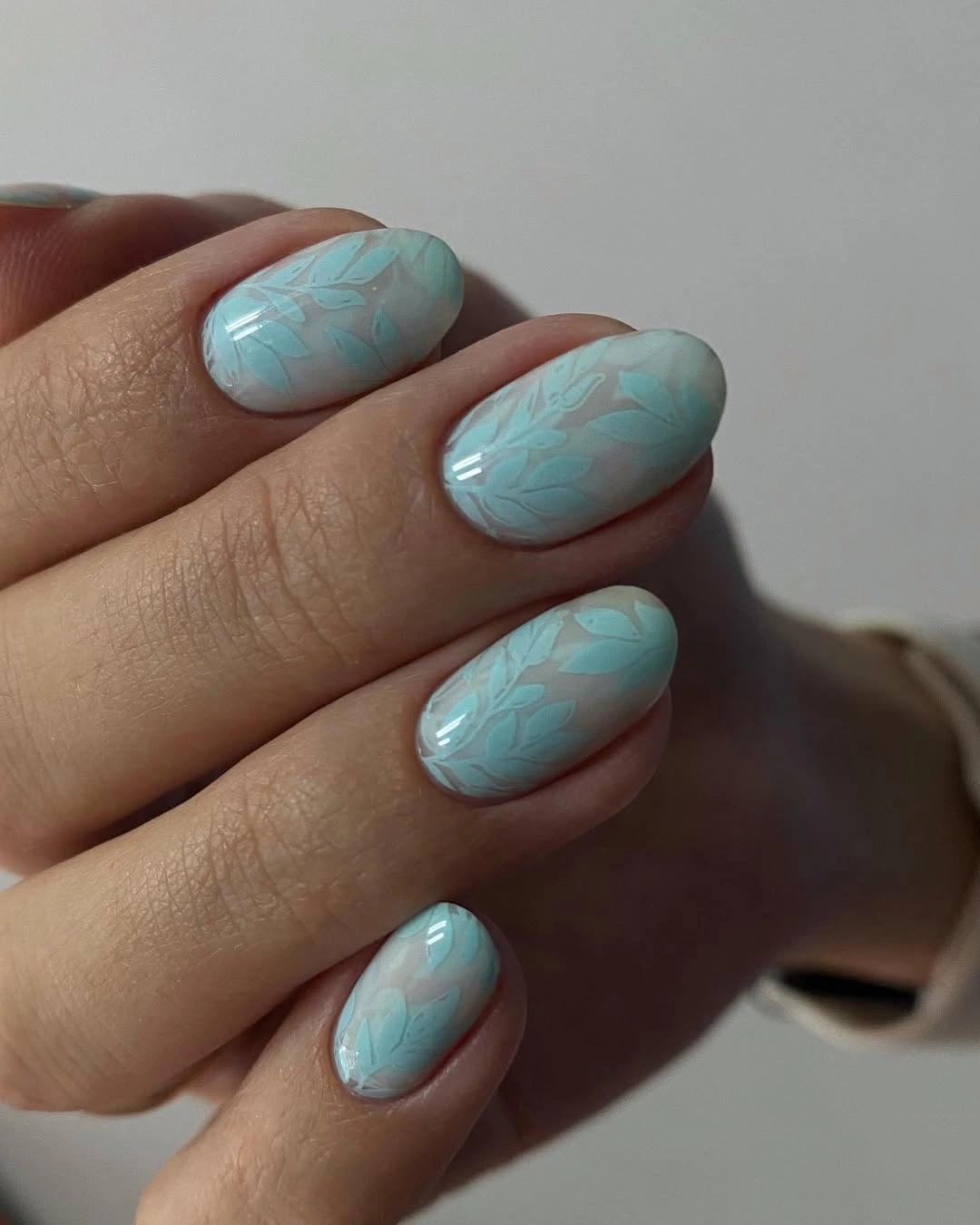 Short oval aqua nails with subtle leaf-like patterns