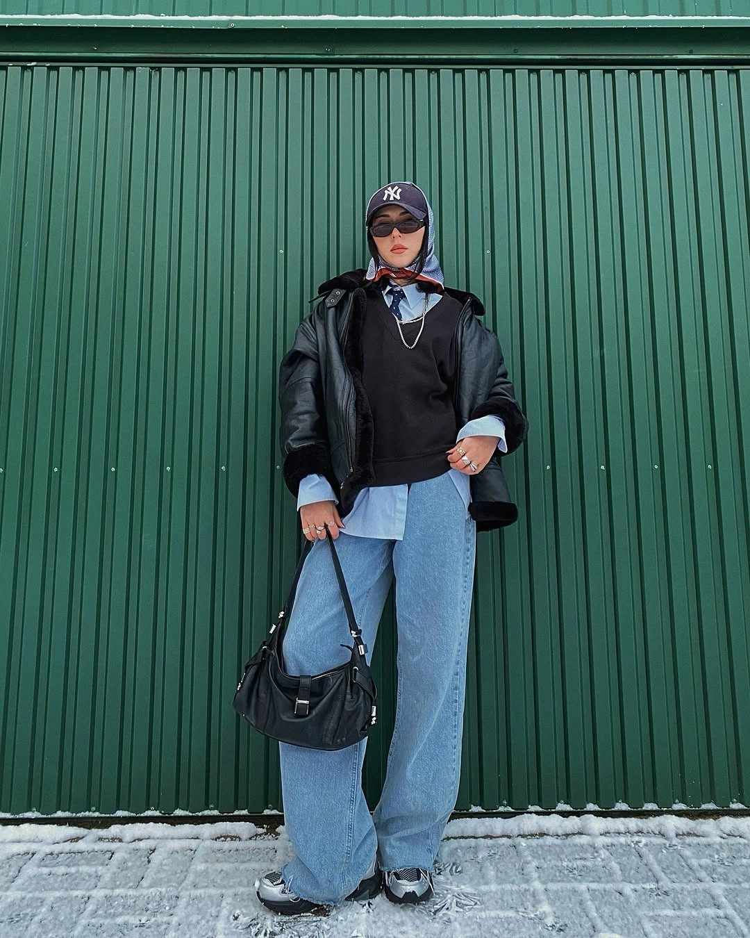 black cap and jacket over pale blue long shirt hem loose blue jeans and metallic shoes