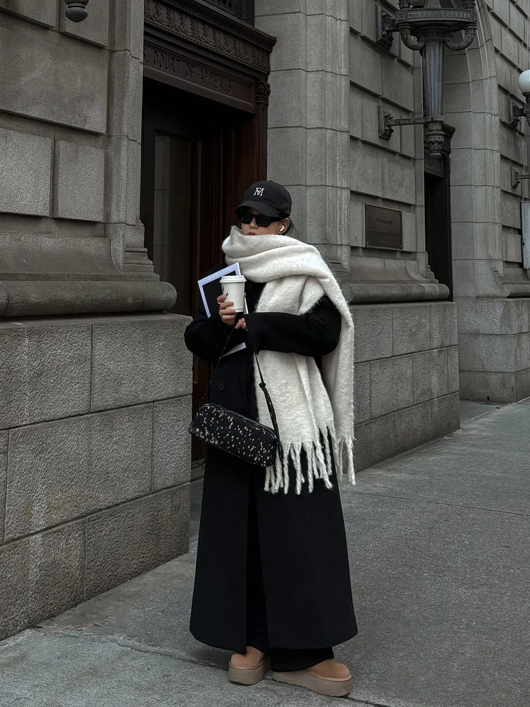 long black coat with oversized ivory fringed scarf black cap and tan shoes