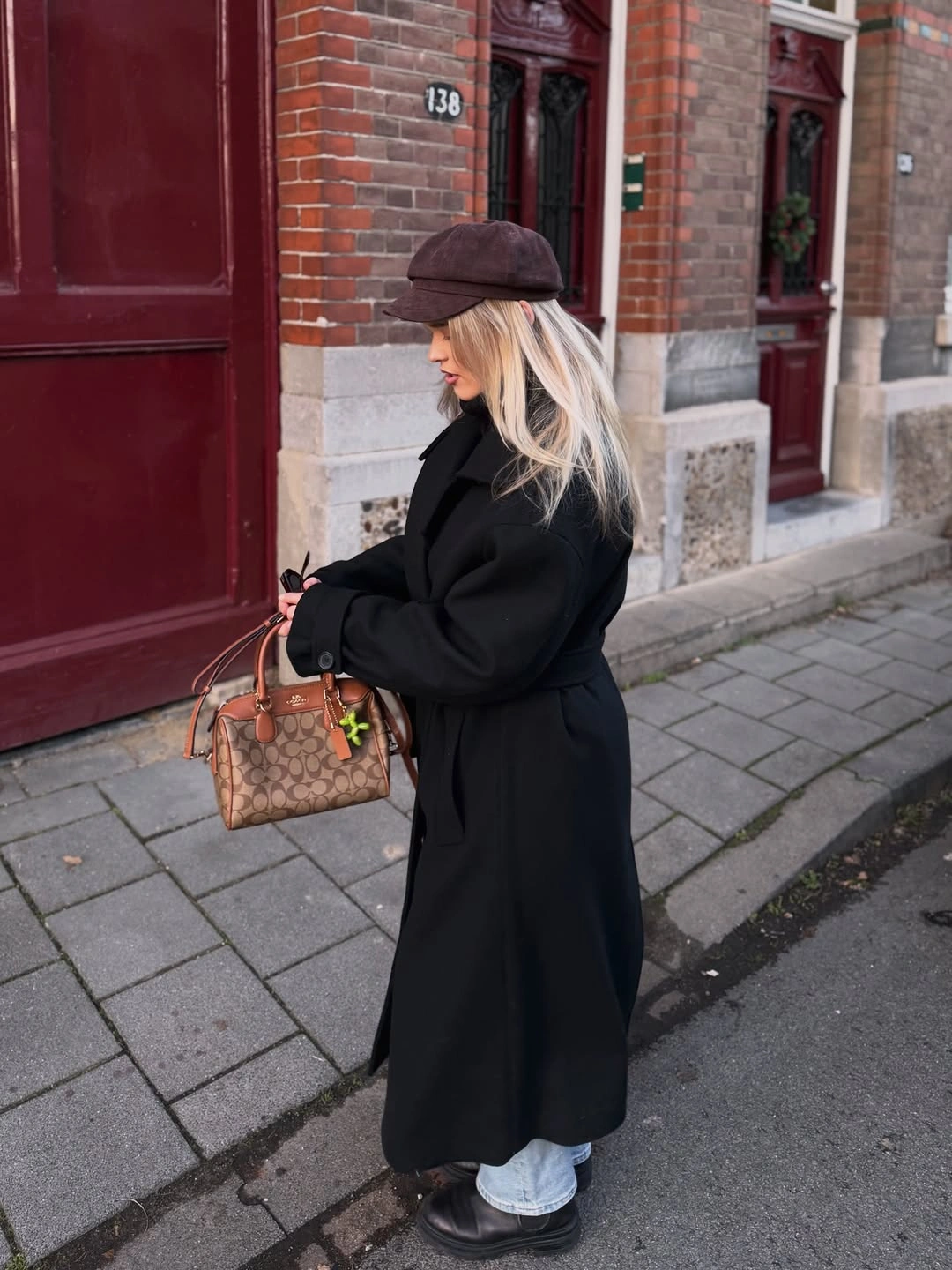 long black coat with white wide trousers dark cap black shoes and brown handbag