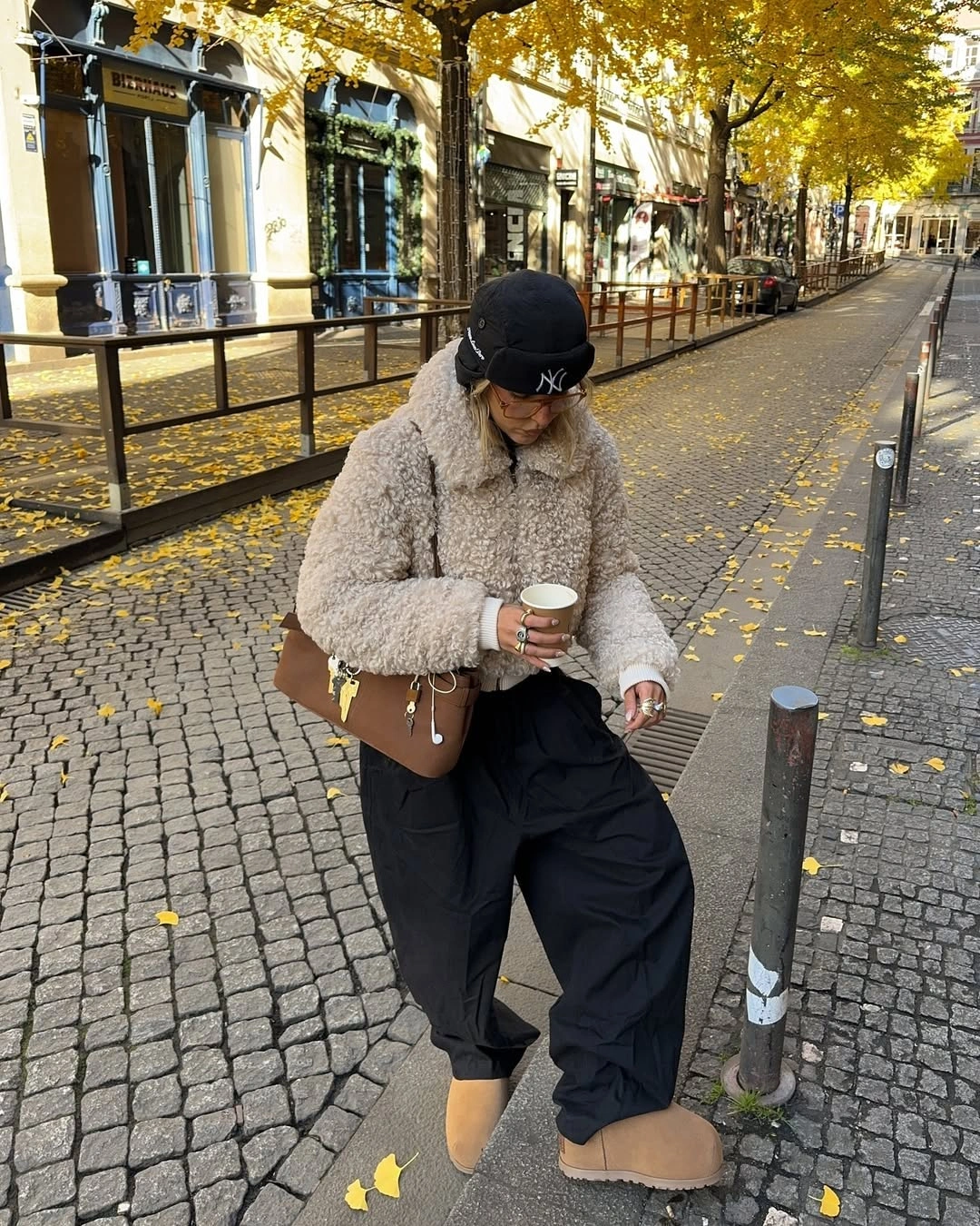 beige textured teddy jacket with black cargo pants tan boots dark cap and brown bag