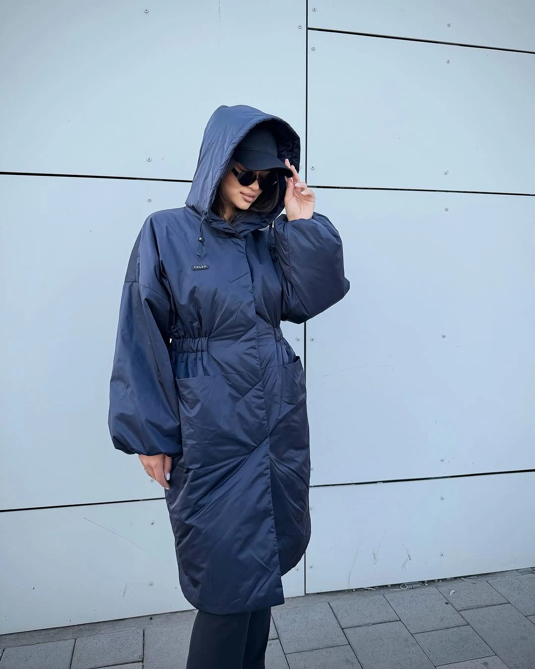 long cobalt blue hooded puffer with gathered waist black wide pants and sunglasses