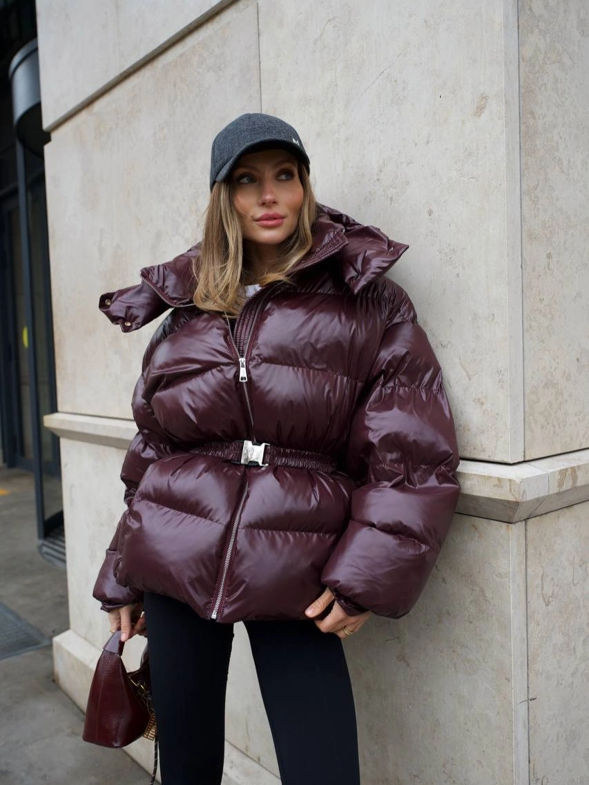 glossy burgundy belted puffer with black cap black trousers and brown bag